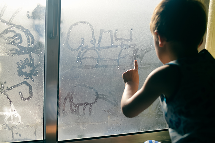 Jeune enfant dessinant sur une fenêtre enbumée